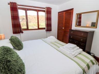 A bedroom with a bed with green pillows and towels on it a chest of drawers with a mirror and a window with red plaid curtains at Green Hills Farm in Ulverston