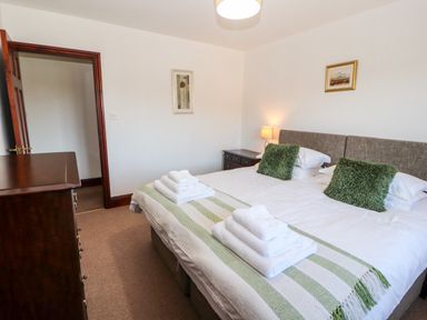 A bedroom with a double bed and green pillows folded towels on the bed a wooden dresser and bedside table at Green Hills Farm in Ulverston