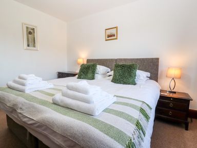 A bedroom with a double bed green pillows bedside tables with lamps and folded towels at Green Hills Farm in Ulverston