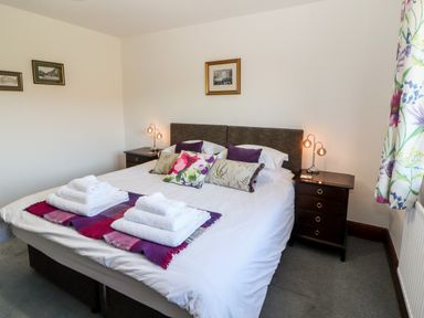 A bedroom with a double bed pillows nightstands lamps and folded towels at Green Hills Farm in Ulverston