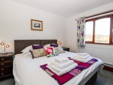 A bedroom with a bed with pillows and folded towels on a blanket near a window with floral curtains at Green Hills Farm in Ulverston