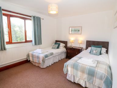 A bedroom with two single beds a wooden nightstand with two lamps between the beds and a window with blue curtains at Green Hills Farm in Ulverston