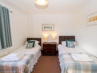 A bedroom with two single beds with plaid blankets and pillows a nightstand with lamps and a duck figurine a painting and curtains at Green Hills Farm in Ulverston