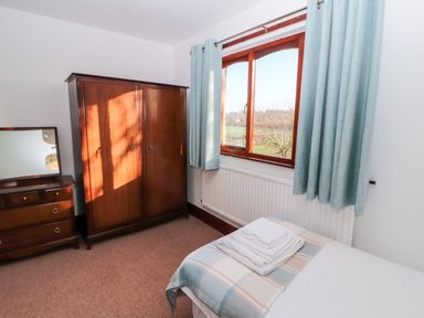 A bedroom with a wooden wardrobe, dresser with mirror, bed with folded towels and window with curtains at Green Hills Farm in Ulverston