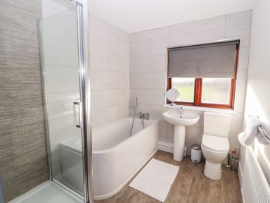 A bathroom with a bathtub shower sink toilet and a window with grey blind at Green Hills Farm in Ulverston