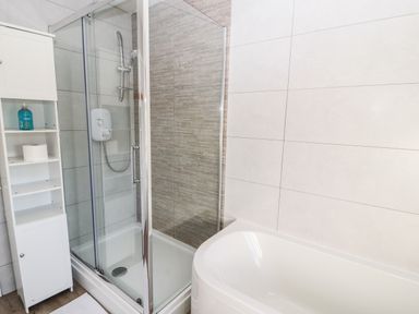 A bathroom with a glass shower enclosure a white bathtub and a white shelving unit at Green Hills Farm in Ulverston