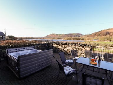 An outdoor patio with a hot tub a glass table with chairs and a stone wall with hills in the background at Green Hills Farm in Ulverston