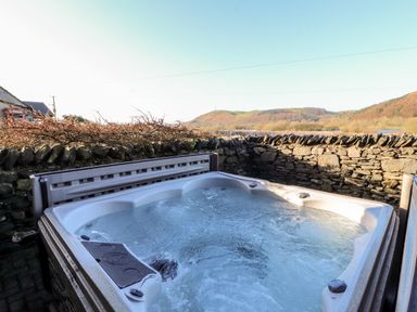 An outdoor hot tub with bubbling water next to a stone wall and hills in the background at Green Hills Farm in Ulverston