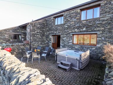 An outdoor patio area with a hot tub a table with six chairs and a stone wall at Green Hills Farm in Ulverston
