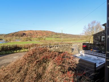An outdoor area with a hot tub table chairs a barbecue and stone walls with fields and hills in the background at Green Hills Farm in Ulverston