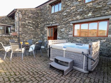 An outdoor patio area with a hot tub and a table with chairs outside a stone building at Green Hills Farm in Ulverston