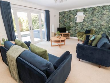 A living room with blue sofas green armchair round wooden coffee table and glass doors with garden view at The Croft in Longhoughton near Alnwick