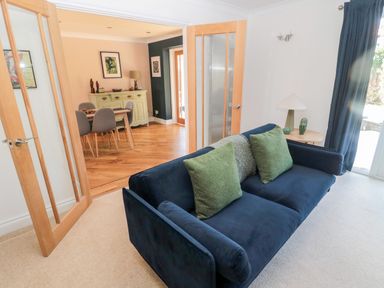 A living room with a blue sofa with green cushions and a side table with a lamp and decor next to glass doors leading to a dining area at The Croft in Longhoughton near Alnwick