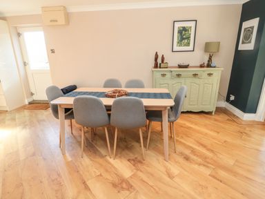 A dining room with a wooden table and six grey chairs a sideboard with decorative items and framed pictures on the wall at The Croft in Longhoughton near Alnwick