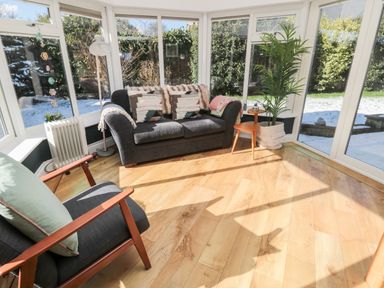 A sunroom with a sofa a chair a floor lamp a side table a plant and wooden flooring at The Croft in Longhoughton near Alnwick