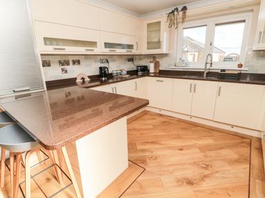 A kitchen with white cabinets brown countertops wooden floor and stools at The Croft in Longhoughton near Alnwick