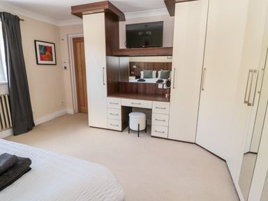 A bedroom with built in wardrobe cabinets a vanity desk with a stool a mounted television and a bed with towels on it at The Croft in Longhoughton near Alnwick