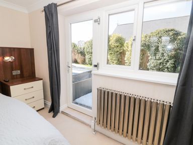 A bedroom corner with a bedside table and lamp next to a glass door and window with a radiator below at The Croft in Longhoughton near Alnwick