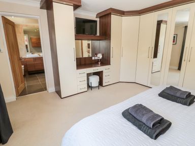 A bedroom with built in wardrobes a vanity area with a mirror and a television a bed with folded towels and an open door showing a bathroom at The Croft in Longhoughton near Alnwick