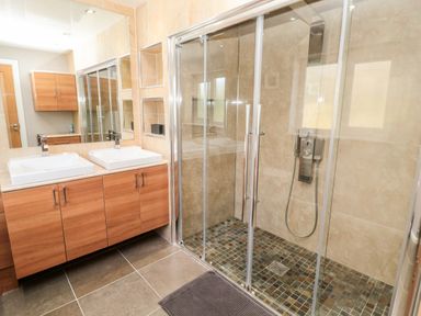 A bathroom with double sinks wooden cabinets a glass-enclosed shower and tiled floor at The Croft in Longhoughton near Alnwick