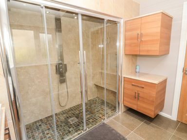 A bathroom with a glass-enclosed shower and wooden cabinets at The Croft in Longhoughton near Alnwick