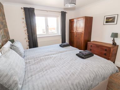 A bedroom with two single beds side by side a wooden wardrobe and chest of drawers with a lamp at The Croft in Longhoughton near Alnwick