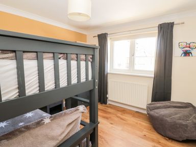 A bedroom with a bunk bed near a window with dark curtains and a bean bag on the wooden floor at The Croft in Longhoughton near Alnwick