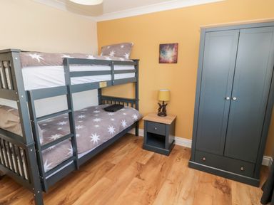 A bedroom with bunk beds a nightstand with a lamp a wardrobe and wooden floor at The Croft in Longhoughton near Alnwick