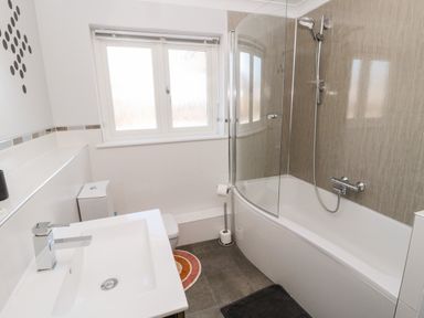 A bathroom with a bathtub shower combination a white sink toilet and window at The Croft in Longhoughton near Alnwick