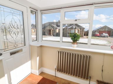 An entryway with a glass front door a radiator a plant on the windowsill and houses visible outside at The Croft in Longhoughton near Alnwick