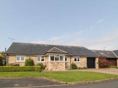 A stone bungalow with a lawn driveway and bushes at The Croft in Longhoughton near Alnwick