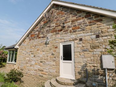 The exterior of a stone house with a white door steps satellite dish and garden plants at The Croft in Longhoughton near Alnwick