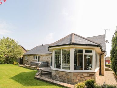 A single story stone house with a slate roof and large windows overlooking a grassy yard at The Croft in Longhoughton near Alnwick