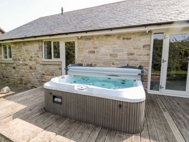 An outdoor hot tub on a wooden deck outside a stone house at The Croft in Longhoughton near Alnwick