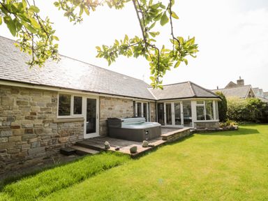 A stone house with a wooden deck and hot tub in a garden with grass and trees at The Croft in Longhoughton near Alnwick