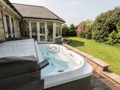An outdoor hot tub next to a stone building with glass doors and a grassy garden with bushes and trees at The Croft in Longhoughton near Alnwick