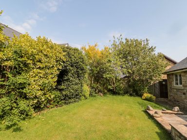 A backyard with grass lawn surrounded by bushes and trees near a stone house at The Croft in Longhoughton near Alnwick