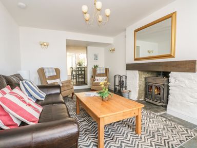 A living room with a leather sofa armchairs a wooden coffee table fireplace and a large mirror at The Watch Below in Polruan