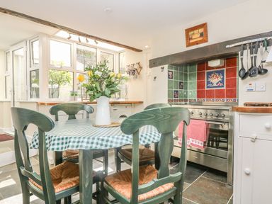 A kitchen with a green checkered tablecloth on a dining table with four chairs and a vase of flowers on top at The Watch Below in Polruan