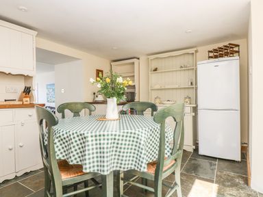 A kitchen with a round table covered with a green and white checkered tablecloth and four green chairs at The Watch Below in Polruan