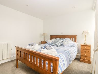 A bedroom with a wooden bed with striped bedding and pillows two wooden bedside tables with lamps at The Watch Below in Polruan
