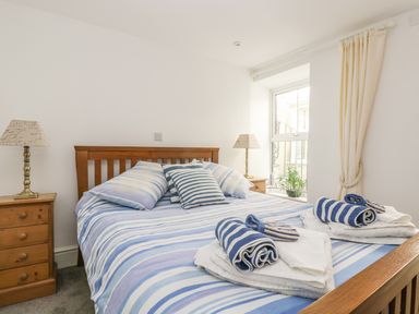 A bedroom with a wooden bed and blue striped bedding with matching pillows two bedside tables with lamps and rolled towels on the bed at The Watch Below in Polruan
