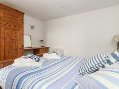 A bedroom with a striped blue and white bedspread wooden wardrobe wooden desk and a lamp at The Watch Below in Polruan