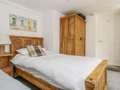 A bedroom with a wooden bed frame, a wooden wardrobe, a lamp on a wooden nightstand, and a painting above the bed at The Watch Below in Polruan