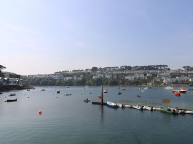 A harbor with boats on the water and houses on a hill in the background at The Watch Below in Polruan