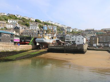 A harbor with boats on a ramp and houses on a hillside at The Watch Below in Polruan