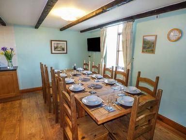 A dining room with a wooden table set for ten with plates glasses and cutlery at Bank End Barn in Grizebeck