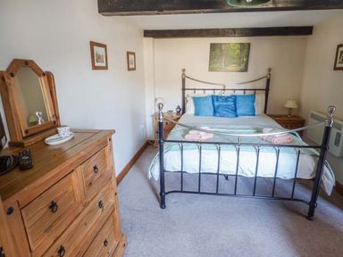 A bedroom with a metal frame bed with blue pillows and wooden furniture including a chest of drawers at Bank End Barn in Grizebeck