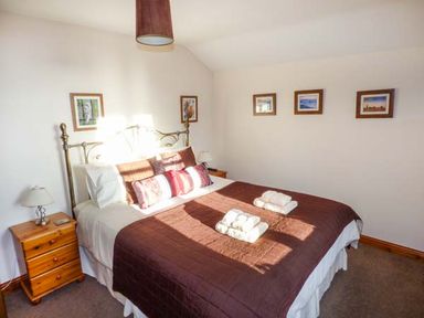 A bedroom with a double bed with folded towels on top and framed pictures on the walls at Bank End Barn Grizebeck