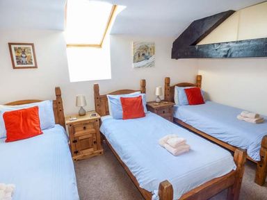 A bedroom with three single beds with blue bedding and red pillows with wooden nightstands under a skylight at Bank End Barn in Grizebeck